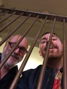 Left to Right:  Doug Holder with Jack Holland behind the bars of an old bank vault at the Bloc 11 Cafe in Somerville, Mass.